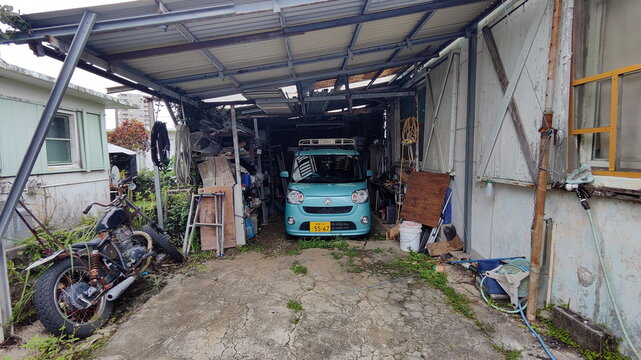 Urasoe, Japan - May 14, 2026. Open Garage with Daihatsu Canbus and Old Motorcycle at Minatogawa
