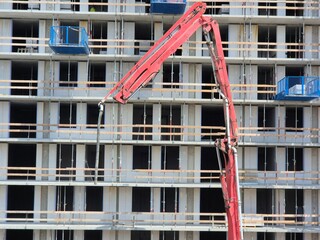 ertical boom and hose of a concrete pump truck in front of a residential building structure under construction with outrigger platforms. © Mevhis