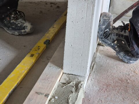 Construction workers holding the bottom of a newly installed wall with their feet, with a spirit level placed on the floor.