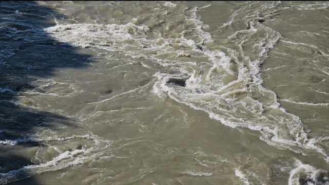 Top-down perspective of turbulent, muddy water currents creating vortexes and whirlpools