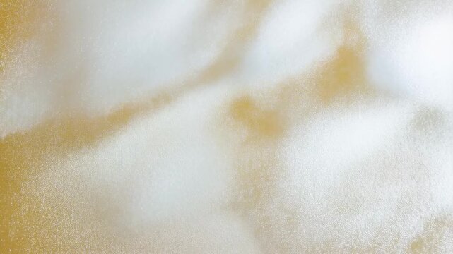 Slow motion macro pan and subtle zoom of gold powder dispersing and settling over white textured surface on tabletop studio backdrop close up