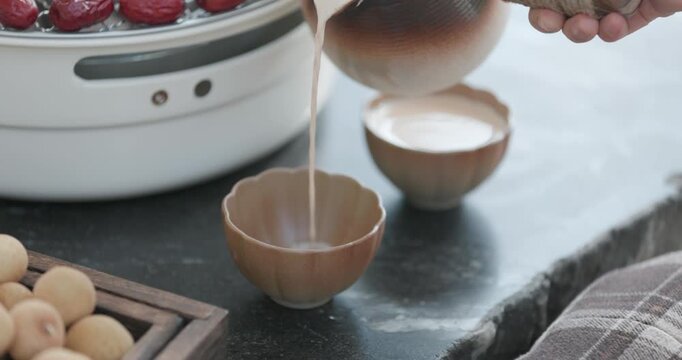 Pouring Warm Milk into Ceramic Bowl with Dried Fruit and Snacks