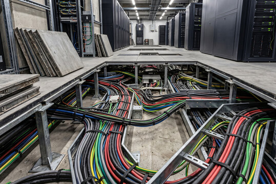 Raised floor in a data center revealing colorful heavy power cables and wiring trays