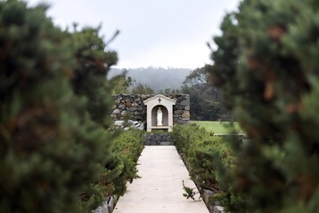 Naklejka premium a sacred minimal outdoor healing scene centered on a small Marian grotto niche seen from a distance, inviting silent prayer