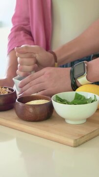 Vertical video: Reaching hands with smartwatch grinding in mortar on board, cutting lemon for prep