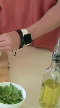 Vertical video: Picking up oil bottle, woman in coral top preparing spinach at counter with lemon