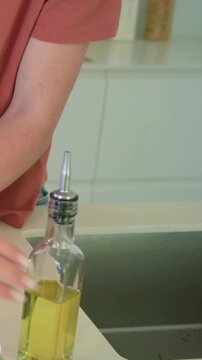 Vertical video: Placing mortar, cook in peach top crushing herbs at counter taking oil for dressing