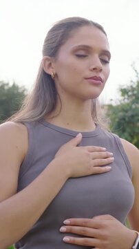 Vertical video: Breathing woman hands-chest-belly, calming in garden, tank, smartwatch, gold hoops