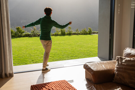 Sliding glass door opening onto sunlit lawn, leather sofa showing textured pillows and orange throw