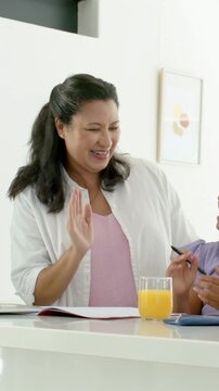 Vertical video: Leaning mum in white guiding child with workbook as child pointing at home counter