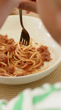 Vertical video: Pressing black fork, diner twirling spaghetti from bowl eating at table, with basil