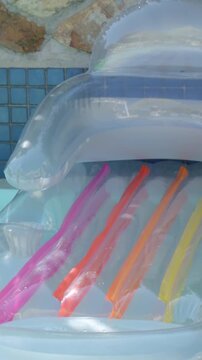 Vertical video: Bobbing inflatable lounger catching sun by pool edge, showing six colored tubes