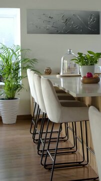 Vertical video: Panning camera left across island and stools in kitchen, showing palm and daylight