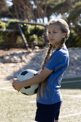 Naklejka premium Child girl posing on turf holding black-white soccer ball wearing blue shirt and shorts, copy space