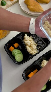 Vertical video: Reaching blue-top cook scooping rice from jar into meals at home with cucumber