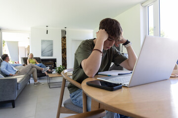 Obraz premium Family with teenage son sitting at dining table in living room working on laptop and notebook