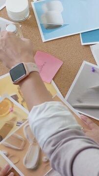 Vertical video: Cue guiding stylist hands wearing top placing prints on corkboard testing bottles