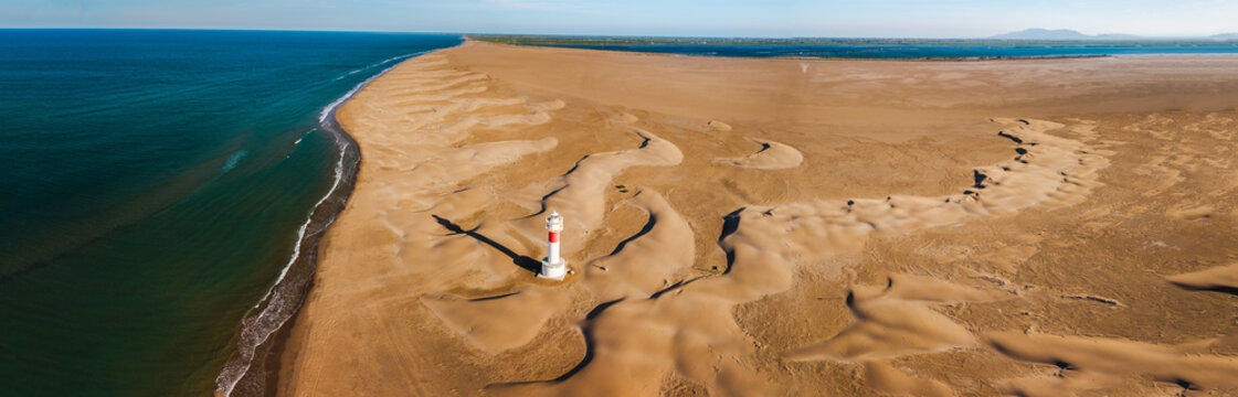 Aerial view of Fangar Lighthouse surrounded by coastal sand dunes and Mediterranean shoreline in the Ebro Delta