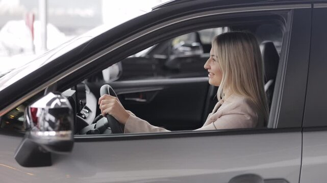 Happy business woman sitting in new car at dealership showroom