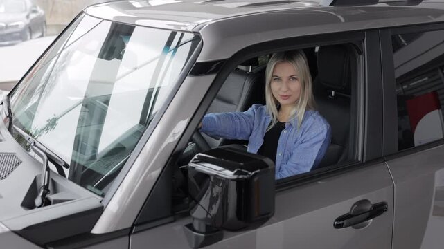 Happy business woman sitting in new car at dealership showroom