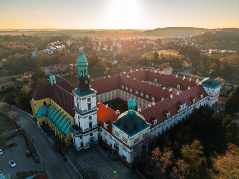 Drone aerial view of the Sanctuary of Saint Hedwig in Trzebnica, Poland, featuring the historic baroque basilica and monastic complex at sunset.