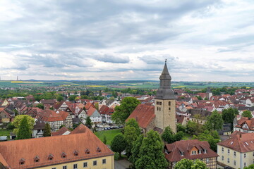 Obraz premium Blick über die Dächer der historischen Altstadt von Hofgeismar mit der markanten Altstädter Kirche im Zentrum, umgeben von grünen Bäumen und sanften Hügeln unter bewölktem Himmel.