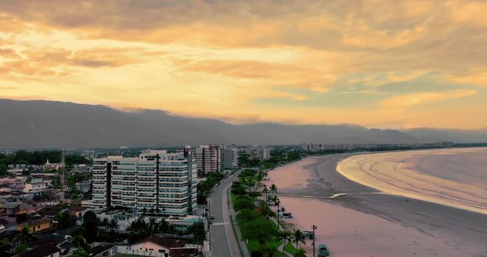 4K aerial view of downtown Bertioga at sunset, featuring waterfront, urban landscape, coastal scenery and mountains in the background.