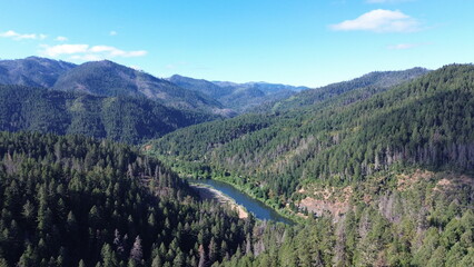 Drone view of a clear river peeking around the valley floor amongst rolling forested hills in the pacific northwest on a early summer morning. © Chanse