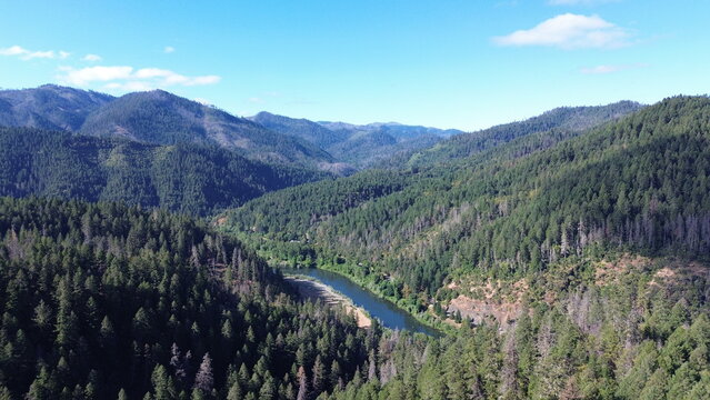 Drone view of a clear river peeking around the valley floor amongst rolling forested hills in the pacific northwest on a early summer morning.