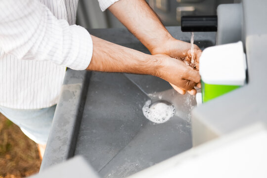 Close-up of a man washing hands with water at an outdoor portable sink. Essential hand hygiene procedure for disease and infection prevention during travel or at a campground.