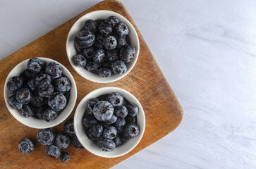 Fresh blueberries in white bowls on wooden cutting board, top view copy space. Healthy organic food concept. © BrayanEfrain