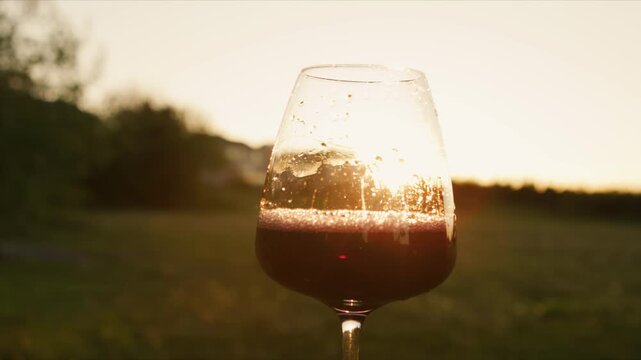 Enjoy the beauty of red wine being poured into a glass, backlit by a stunning sunset. A perfect moment captured at a tranquil winery, inviting relaxation