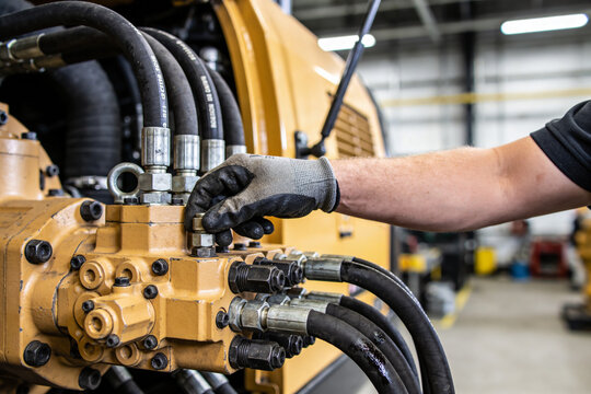 Mechanic's gloved hand adjusting hydraulic lines on heavy construction machinery