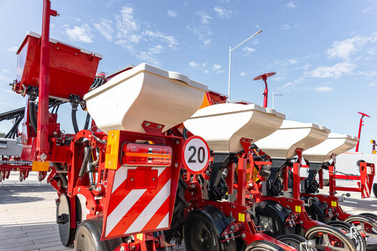 A lineup of red agricultural seed planters parked on a snow-covered field under a clear blue sky, showing white hoppers, wheels, metal frames and reflective