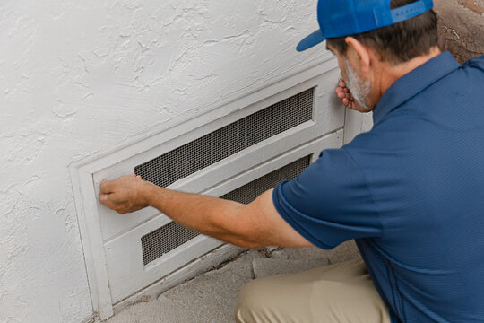 A home inspector is opening a crawl space access hatch underneath a residential home