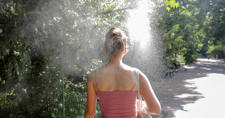 Naklejka premium Young woman cooling down with water mist spray in park
