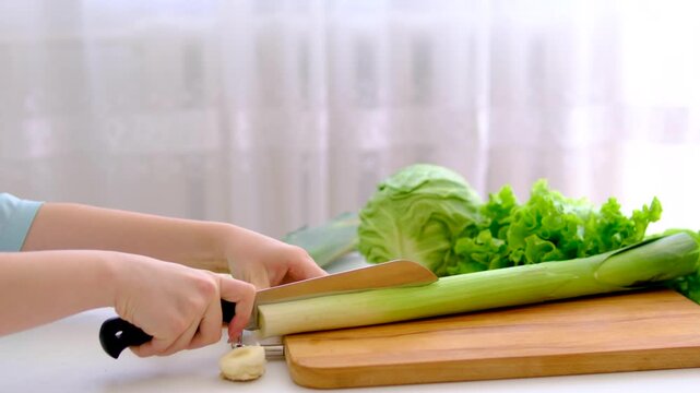 Chopping green leek stems in minimal white kitchen with fresh cabbage and salad leaves