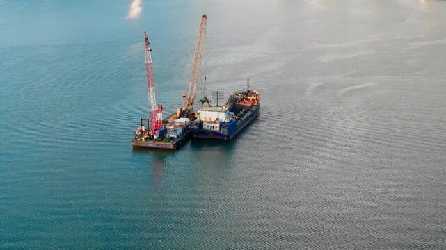 Dredging vessel and crane platform operating in calm coastal water. Aerial view of marine equipment used for seabed excavation and sediment removal