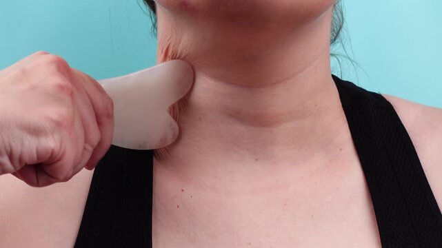 Woman massaging neck with rose quartz gua sha tool to treat rings of Venus wrinkles. Anti-aging lifting massage for tech neck skin rejuvenation.