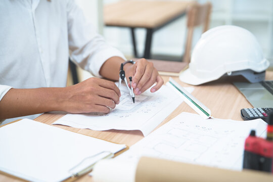 Architect or engineer working on building plans with drafting tools, calculator, and helmet