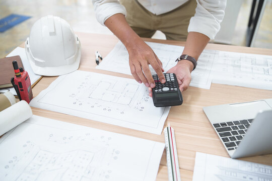 Construction Professional Using Calculator on Architectural Plans for Project Management