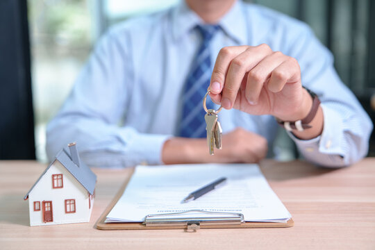Real estate agent handing over keys with a model house and contract for property ownership transfer