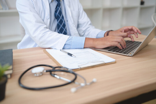 Medical Professional Typing on Laptop While Working with Patient Records and Stethoscope