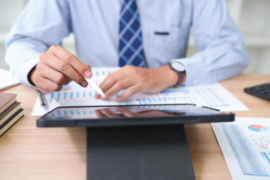 Businessman Analyzing Financial Data on Digital Tablet and Papers in Office
