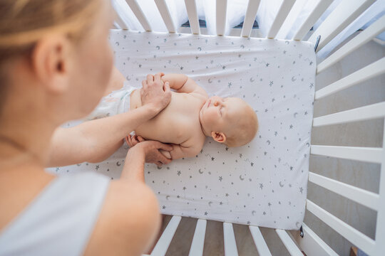Mother gently placing sleeping baby into crib at home. Caring mom putting newborn to bed with tenderness and love. Bedtime routine, parenting care, early childhood and family bonding concept