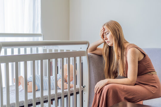 Very tired mother sitting by baby crib at home feeling exhausted. Sleep deprived mom caring for newborn at night. Parenting fatigue, motherhood stress, childcare and real family life concept