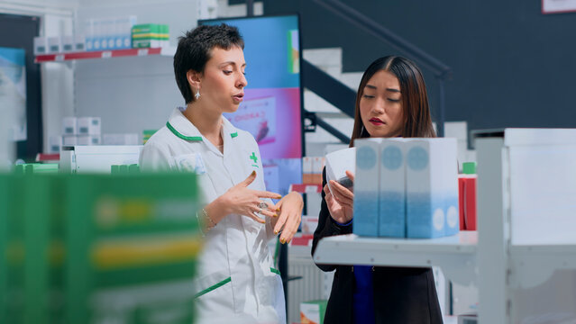 Shopper in pharmacy needing prescription treatment to subdue ache, asking pharmacist to help her pick best medicament, with proficient pharmacologist assisting customer with product insight.