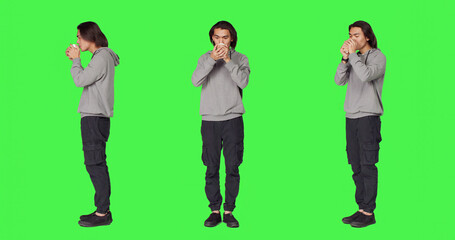 Obraz premium Person drinking coffee on camera, holding cup of hot caffeine beverage over full body green screen template, with young man enjoying refreshment and feeling positive in studio.