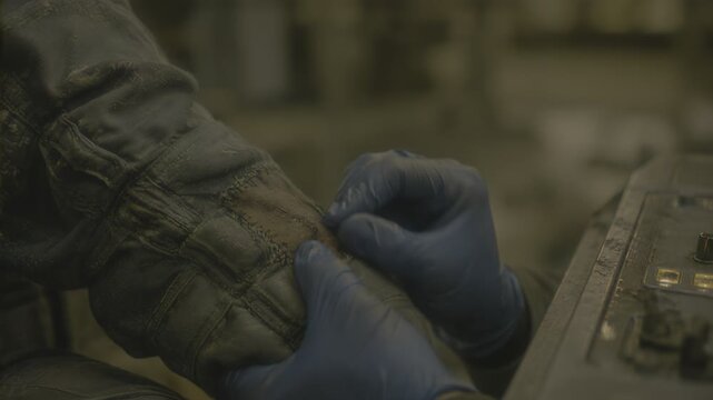 Tailor stitching a patch onto worn clothing. Person using needle and thread to repair fabric garment. Skilled worker mending textile item in industrial workshop.
