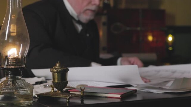 19th century shipwright opens and examines drawings focus on oil lamp